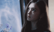 a woman with long hair looks out a window