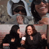two women are laughing in front of a beast tv sign