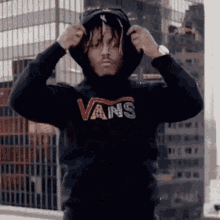 a man wearing a black vans hoodie is adjusting his hood .
