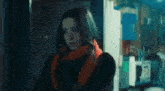 a woman wearing a scarf and a black jacket is standing in front of a window .