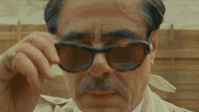 a man with a mustache is wearing sunglasses and a white shirt