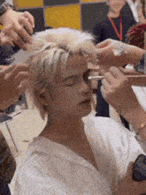 a man with blonde hair is getting his makeup done