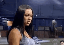 a woman in a gray tank top is standing in a dark room looking at the camera .