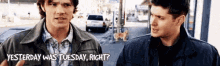 two men are standing next to each other on a street talking about yesterday .