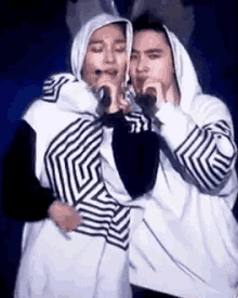a man and a woman are singing into microphones while wearing hoodies .