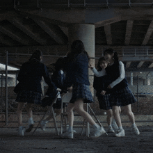 a group of girls in school uniforms are dancing around a chair