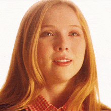 a close up of a woman 's face with long red hair and a plaid shirt