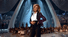 a woman in a tuxedo is standing on a stage with her hands on her hips in front of a crowd .