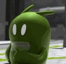 a green cartoon character with two white eyes is standing on a white surface .