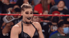 a woman in a black top is standing in a wrestling ring with a crowd watching .
