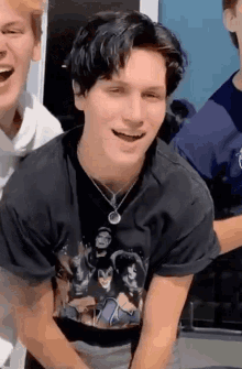 a young man wearing a black t-shirt and a necklace is smiling while sitting next to another man .