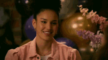 a woman in a pink jacket is smiling in front of balloons .