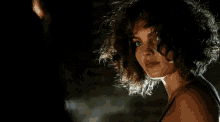 a close up of a woman 's face in a dark room with her hair blowing in the wind .