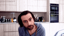 a man with a beard is standing in a kitchen in front of a microwave oven