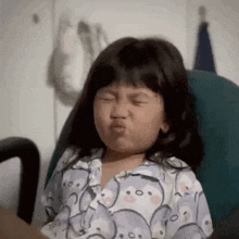 a little girl is sitting in a chair and making a funny face .