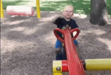 a young boy is riding a red seesaw in a park .