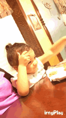 a little girl sitting at a table with her hand on her forehead and a sign that says always