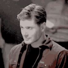 a man wearing a red jacket and a black shirt is standing in a room .