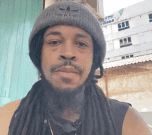 a man with dreadlocks is wearing a grey adidas beanie