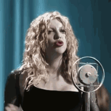 a woman is singing into a microphone with a blue curtain behind her