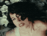 a woman with dark hair and red lips is laying on a bed of white flowers