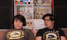 two men sit on a couch with one wearing a shirt that says since