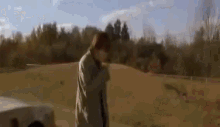 a man is walking down a dirt road next to a car in a field .