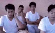 a group of men wearing white shirts are sitting on a bed .