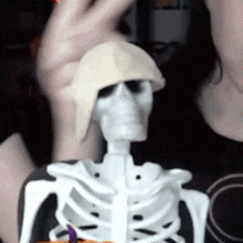 a skeleton wearing a hat is being held by a woman 's hand