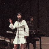 a woman in a white dress is singing into a microphone on stage