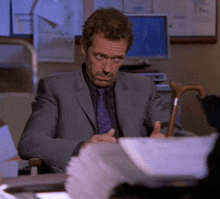 a man in a suit and tie is sitting at a desk with a cane in his hand