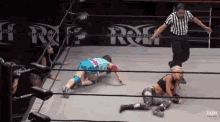 a referee is standing in the middle of a wrestling ring watching two women wrestling .
