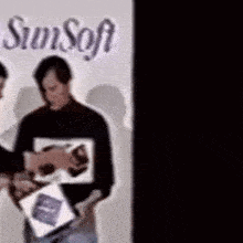 two men standing in front of a sign that says sun soft