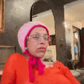 a woman wearing glasses and a pink hat is sitting in front of a mirror in a room .