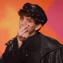 a man wearing a hat with spikes on it covering his nose with his hand