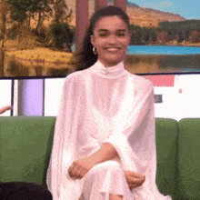 a woman in a white dress is sitting on a green couch .