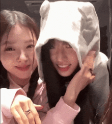 two girls are posing for a picture and one of them is wearing a hoodie with ears .
