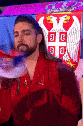 a man with long hair and a beard is standing in front of a flag with the letters ee on it