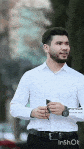 a man with a beard is wearing a white shirt and black pants and a watch