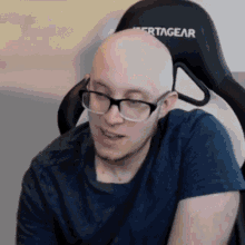 a bald man wearing glasses is sitting in a vertagear gaming chair