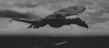 a black and white photo of a dragon flying over the ocean .