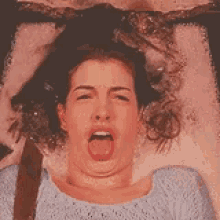 a woman with curly hair is laying on a bed and making a funny face with her hands .