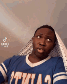 a man in a blue shirt is making a funny face while holding a sheet over his head .
