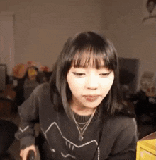 the girl is wearing a black sweater with a cat on it and a necklace around her neck .