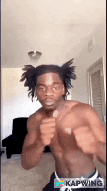 a shirtless man with dreadlocks is dancing in a room with kapwing in the corner .