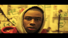 a young man wearing a hooded sweatshirt stands in front of a wall with graffiti on it