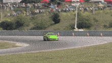 a green car is driving on a race track with a sign that says ' motorsport ' on it