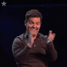a man in a brown shirt is smiling and clapping