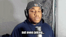 a man wearing headphones and a beanie is talking into a microphone and saying `` not even joking '' .