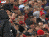a man in a baseball cap stands in front of a crowd with the time of 87:47 on the screen